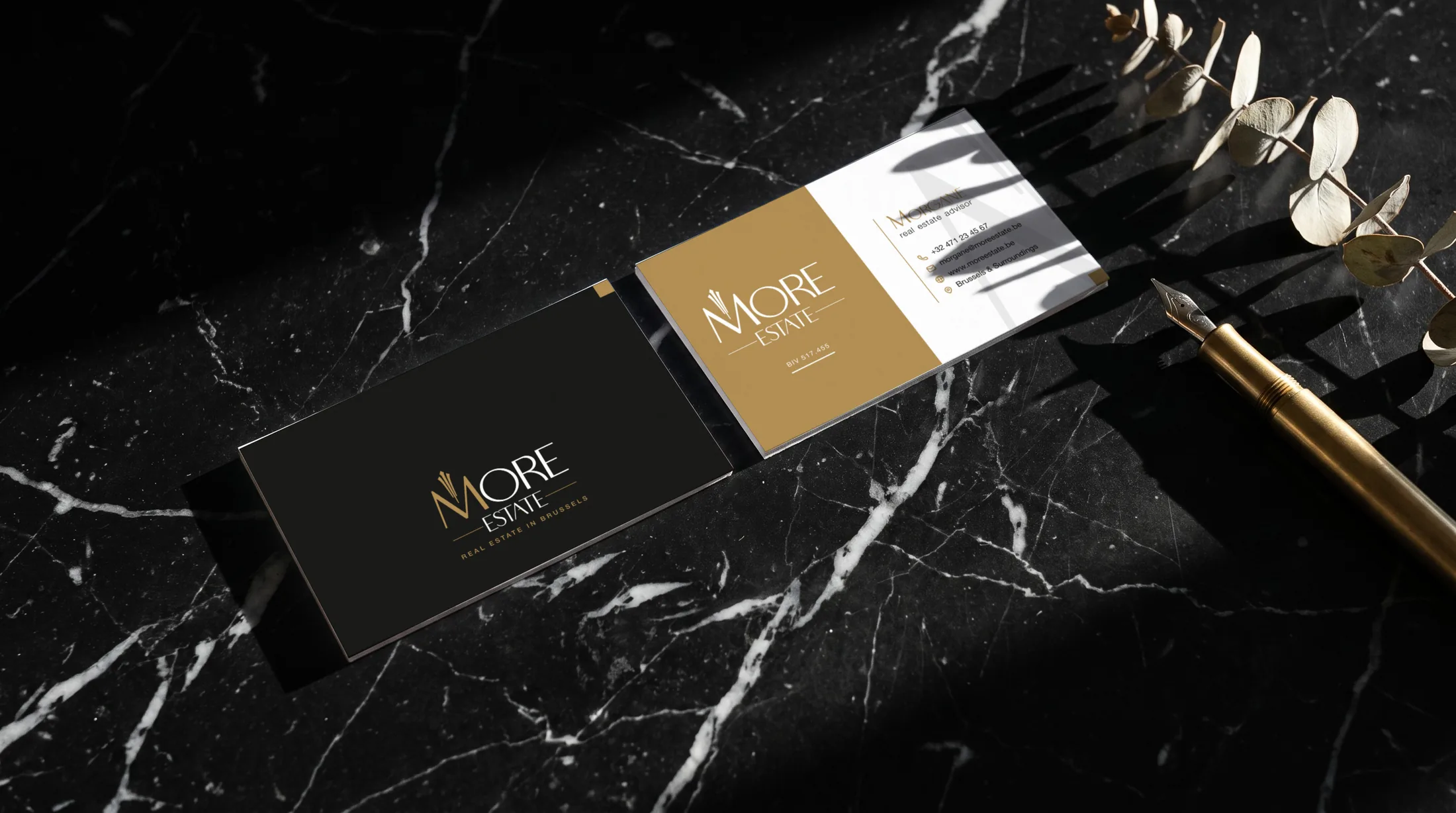 Both sides of the More Estate business card on black marble beside a brass fountain pen